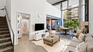 A modern living room with a flat-screen TV, a sofa, a coffee table, and a staircase. - Elegant design meets optimal location amid the natural beauty of Downtown Redmond. (Redmond)