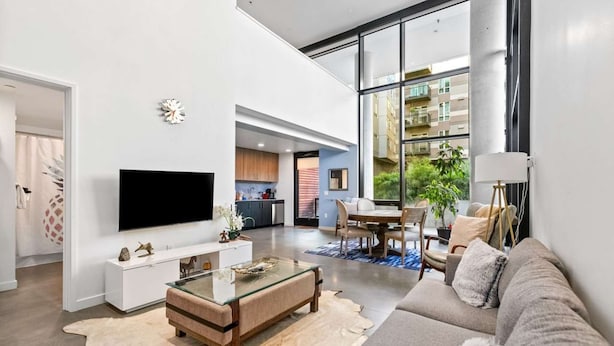 A modern living room with a flat-screen TV, a glass coffee table, a sofa, and a large window offering a view of the city. - Elegant design meets optimal location amid the natural beauty of Downtown Redmond. (Redmond)
