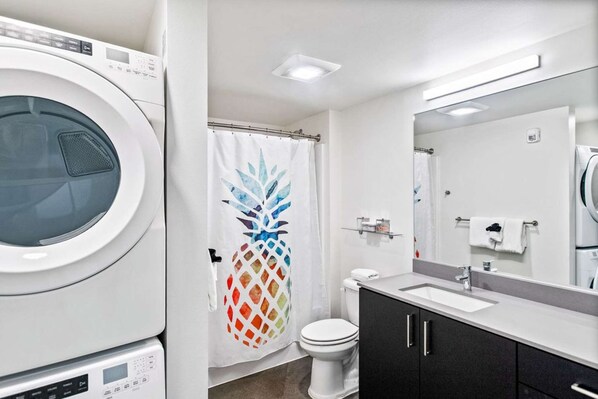 Un baño moderno con lavadora, inodoro, cortina de ducha con diseño de piña, lavamanos y espejo.