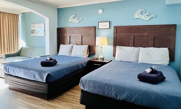 A hotel room with two beds, a nightstand with a lamp, a chair, and a window with curtains. - Comfy Beach View Condo,Pool,B34 (Myrtle Beach)