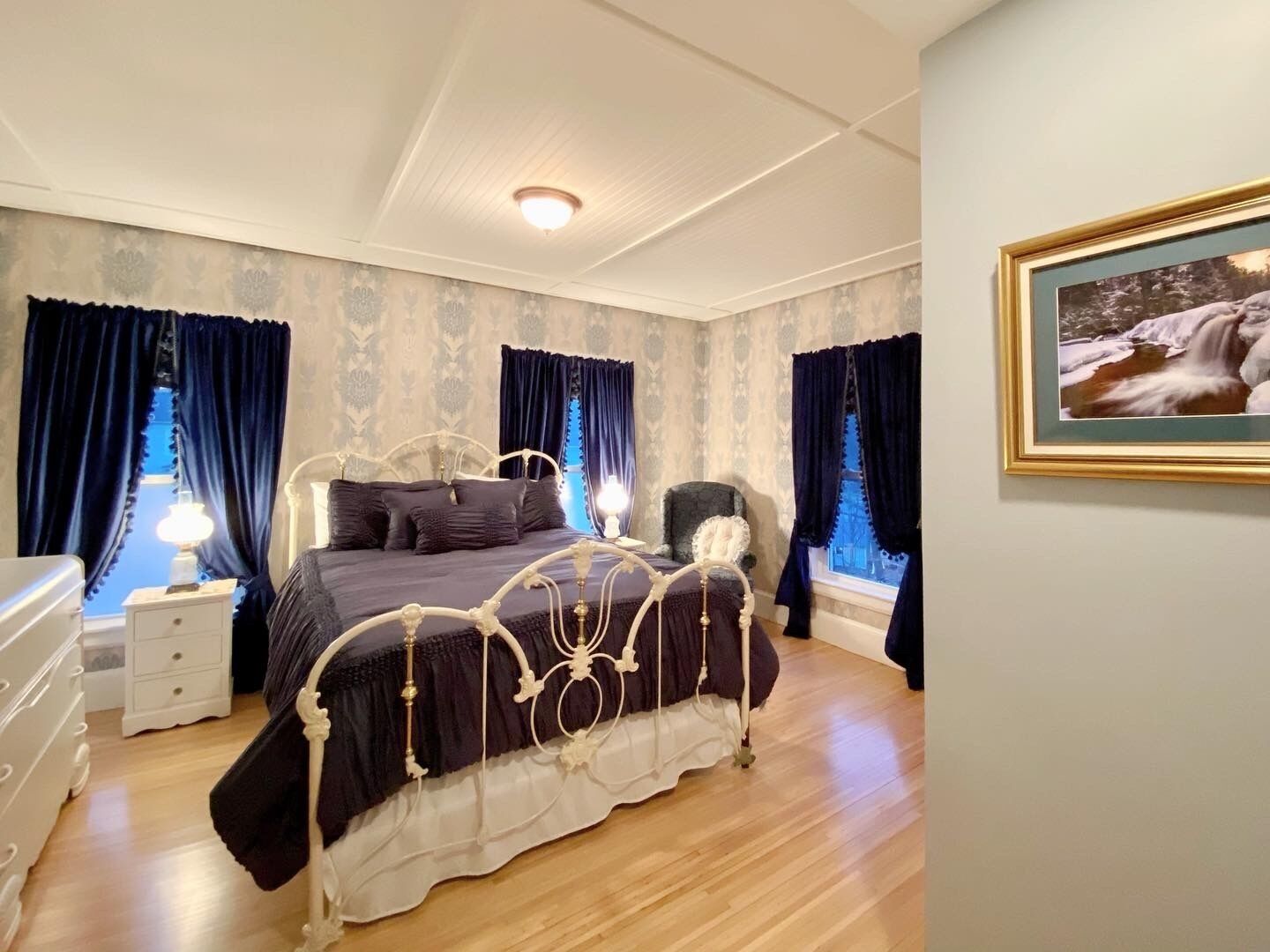 Un dormitorio con una cama grande, una mesita de noche, un aparador y una ventana con cortinas.