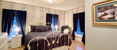 Un dormitorio con una cama grande, una mesita de noche, un aparador y una ventana con cortinas.