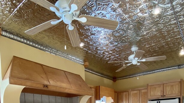 A kitchen with wooden cabinets, a central island, a stove, and a ceiling fan.