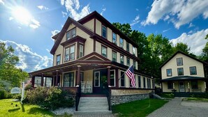A two-story building with a porch, a flag, and a stone foundation.