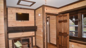 Un intérieur en bois avec une cheminée, un téléviseur fixé au mur et une porte donnant sur l’extérieur.