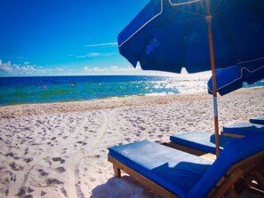 A beach with a blue umbrella and lounge chairs.