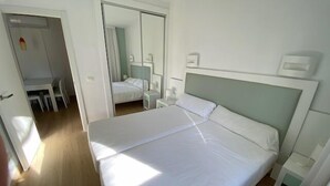 Ein Schlafzimmer mit einem großen Bett, einem Nachttisch, einem Schreibtisch und Stühlen. Eine Tür führt ins Badezimmer und es gibt einen Spiegel.