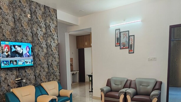 A living room with a blue sofa, a brown sofa, a glass coffee table, and a patterned wall. -  TNV Residency (Puducherry)