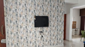 A room with a patterned wallpaper, a mounted television, and a tiled floor. -  TNV Residency (Puducherry)