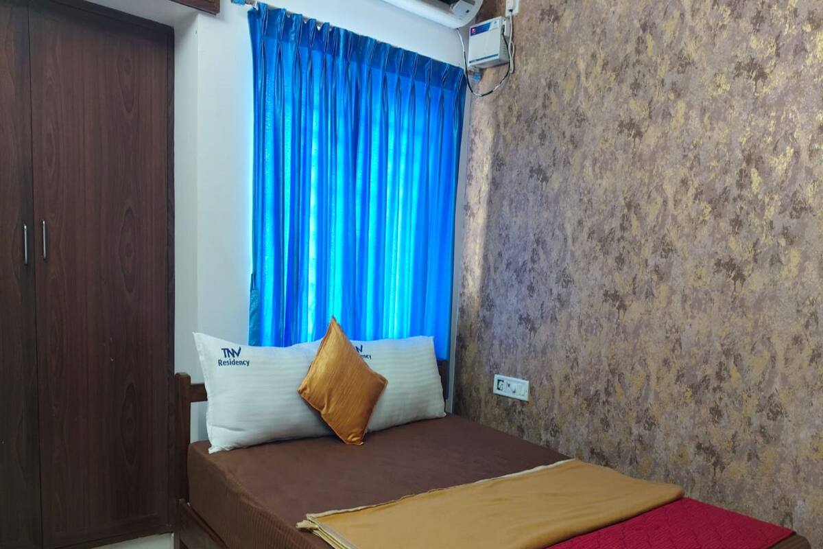A bedroom with a bed, a wardrobe, a window with blue curtains, and a wall air conditioner.