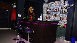 A bar area with a counter, bar stools, and a wall of liquor bottles. -  TNV Residency (Puducherry)