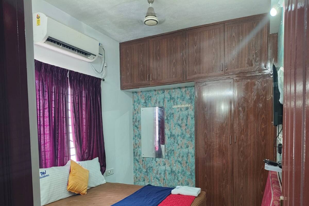 A bedroom with a bed, a wardrobe, a mirror, and an air conditioning unit.