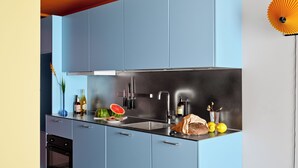 Una cocina moderna con armarios azules, un lavamanos de acero inoxidable y diversos alimentos sobre la encimera.
