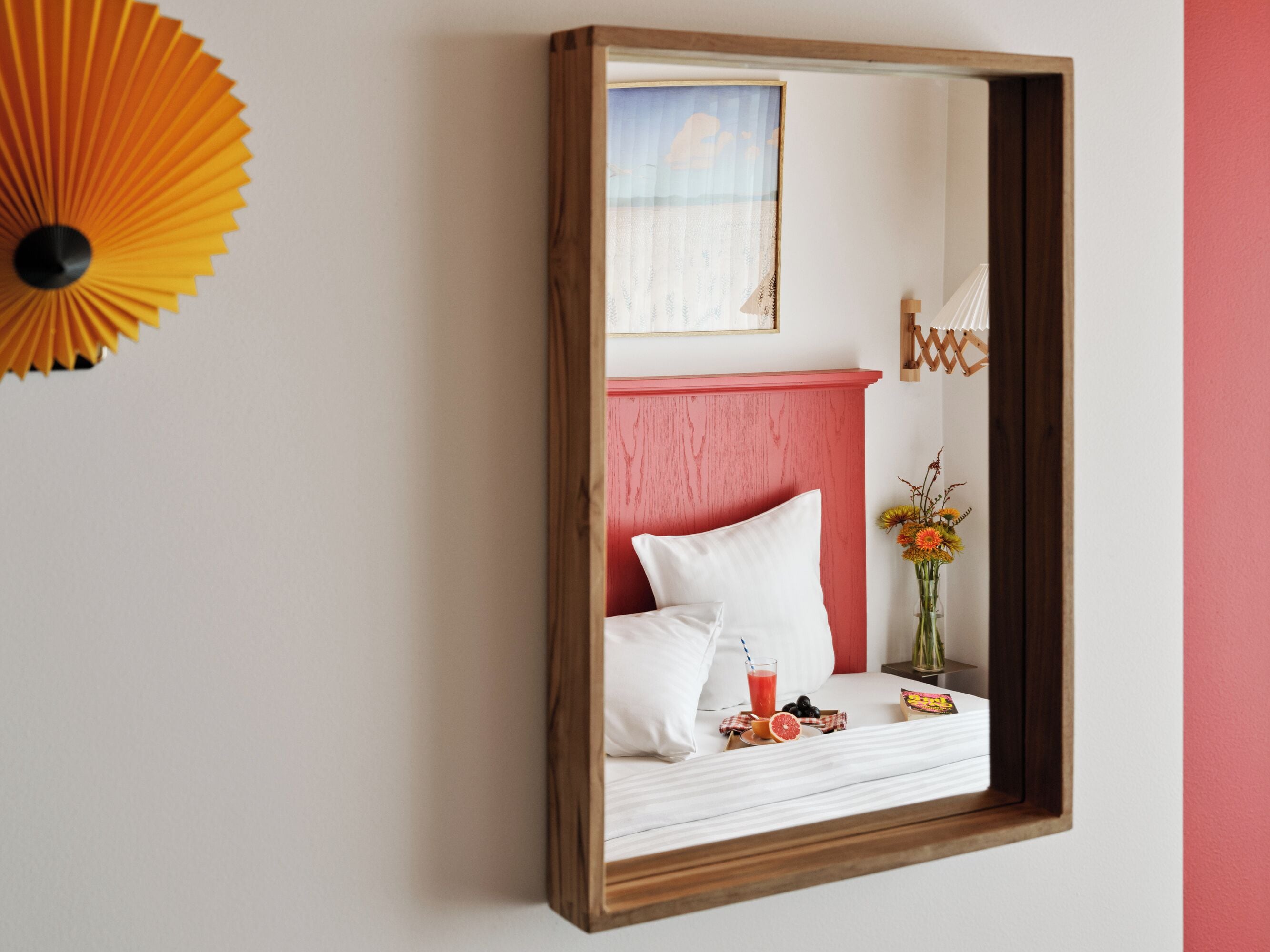 A bedroom with a bed, a bedside table with a glass of juice, and a vase with flowers.