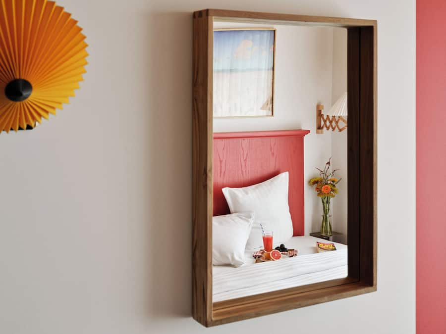 A bedroom with a bed, a bedside table with a glass of juice, and a vase with flowers.