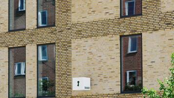 En byggnad med flera våningar, en fasad av tegel och stora fönster. På byggnaden finns en skylt med bokstäverna ”H O A T E L I”, vilket visar att det är ett hotell. Under hotelskylten finns en symbol som föreställer ett nyckelhål.