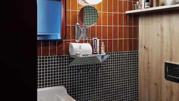 Et badeværelse med en hvid vask, et spejl, et toilet og en hylde med toiletartikler.