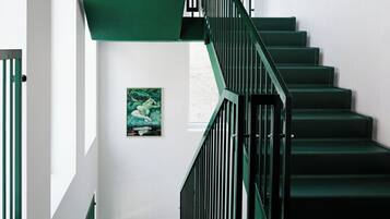 Una escalera con escalones verdes y barandillas negras, que lleva a una plataforma con una obra de arte enmarcada en la pared.