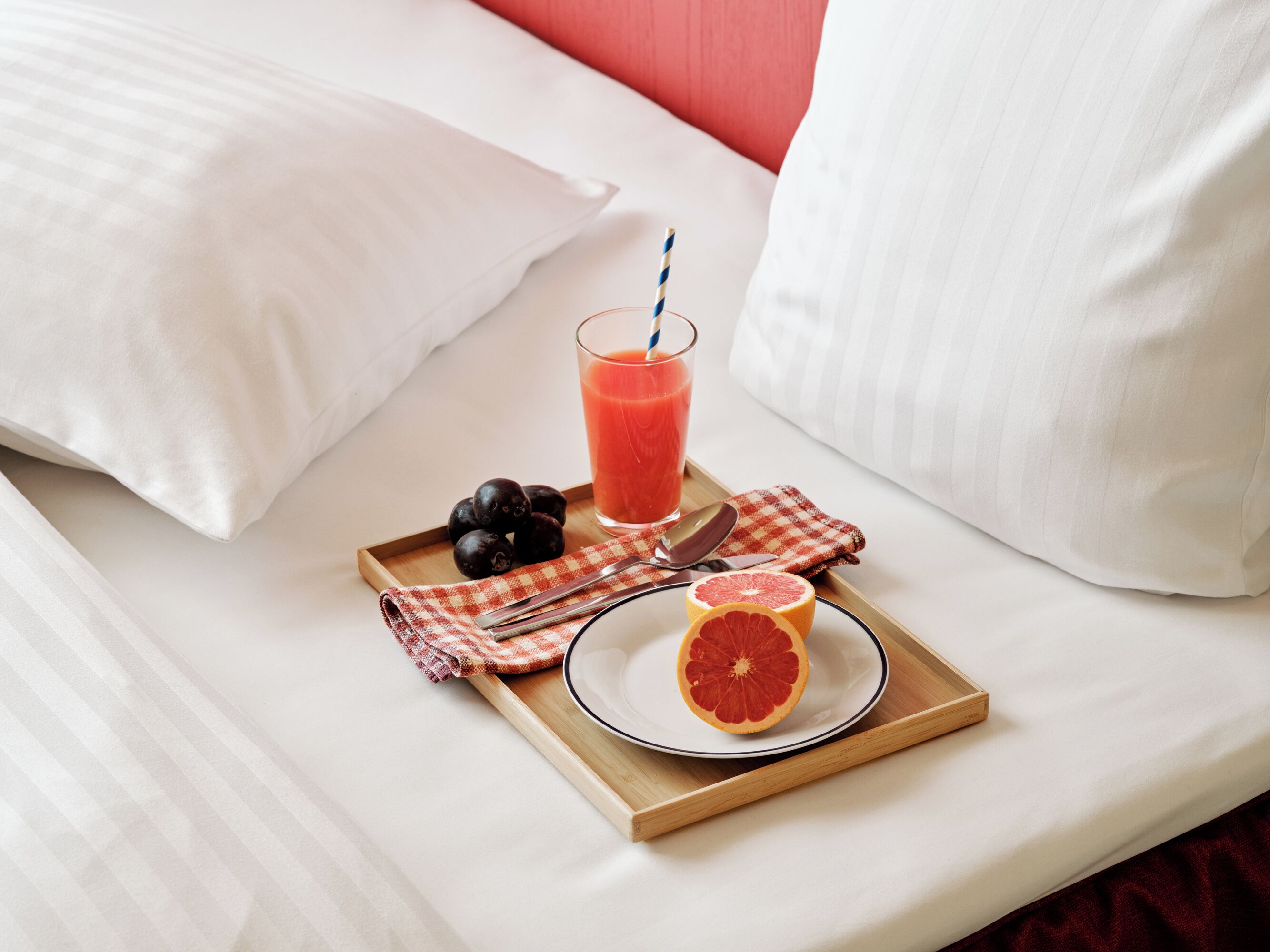 A neatly made bed with white linens, a tray with a glass of orange juice, a plate with a half grapefruit, and a few black olives.