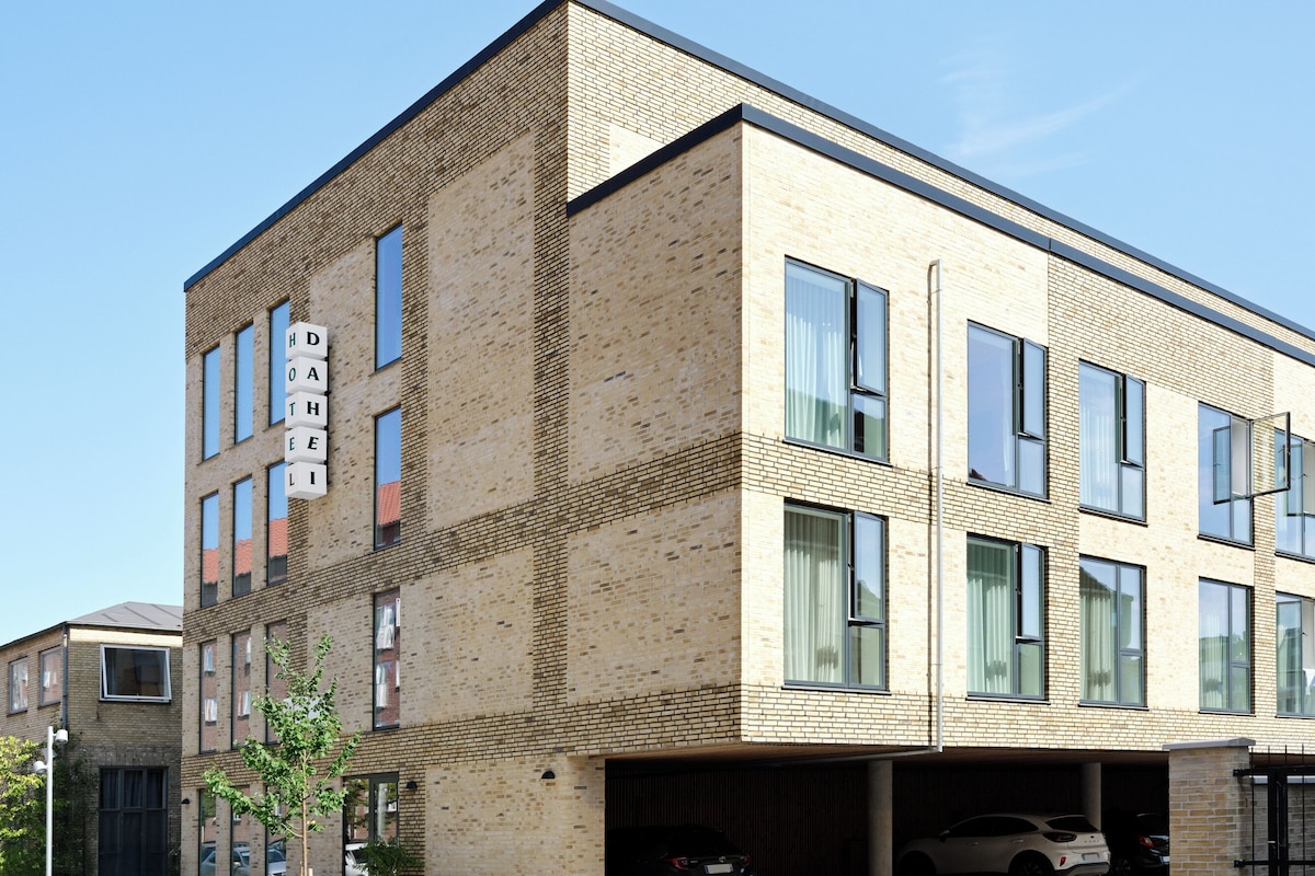 A modern building with a brick facade, multiple windows, and a visible garage area with parked cars.
