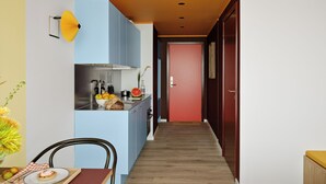 Un pasillo estrecho con una zona de cocina a un lado, un comedor al otro y una puerta roja al final.