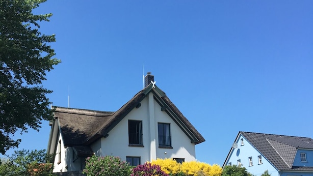 Une maison à deux étages, avec une façade blanche, un toit foncé et une cheminée.