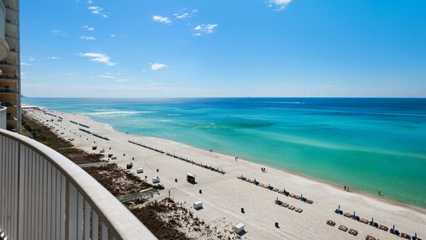 A beach view from a balcony with a clear sky, a sandy beach, and the ocean.