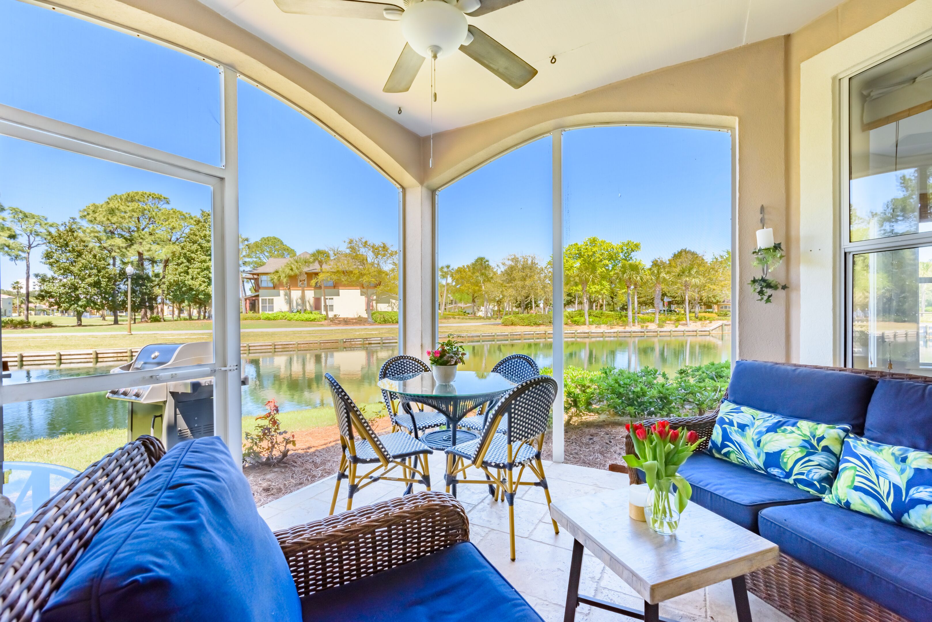 A sunroom with a view of a lake, a dining table with chairs, and a sofa with a vase of flowers.