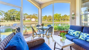 Uma sala de sol com vista para um lago, uma mesa de jantar com cadeiras e um sofá com um vaso de flores.