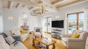Amplia sala de estar con techo de madera, televisor grande y vista a la piscina.