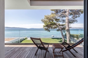 Un balcón con vista al mar, dos sillas de madera y una mesa pequeña.