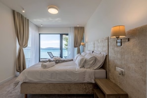 Un dormitorio con cama, lámpara de noche, vista al mar y ventana con cortinas.