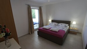 Een slaapkamer met een bed, twee bedlampen, een raam met gordijnen en een vaas met bloemen.