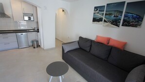 Een moderne woonkamer met een grijze bank, een klein rond tafeltje en een keuken op de achtergrond.