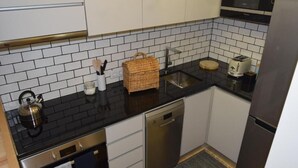 Une cuisine compacte avec des meubles blancs, un plan de travail noir, un lave-vaisselle en acier inoxydable, un four à micro-ondes et un grille-pain.
