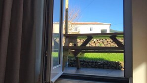 Une pièce dotée d’une porte-fenêtre coulissante qui donne sur un espace extérieur agrémenté d’une pergola en bois et offrant une vue sur un bâtiment blanc avec un toit en tuiles.