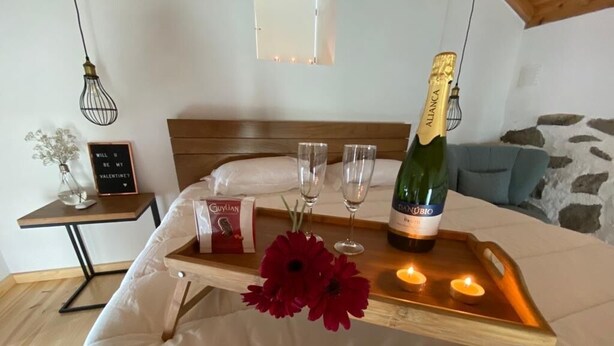 Un lit avec une table de chevet sur laquelle se trouvent une bouteille de champagne, deux verres et un plateau orné de fleurs rouges.