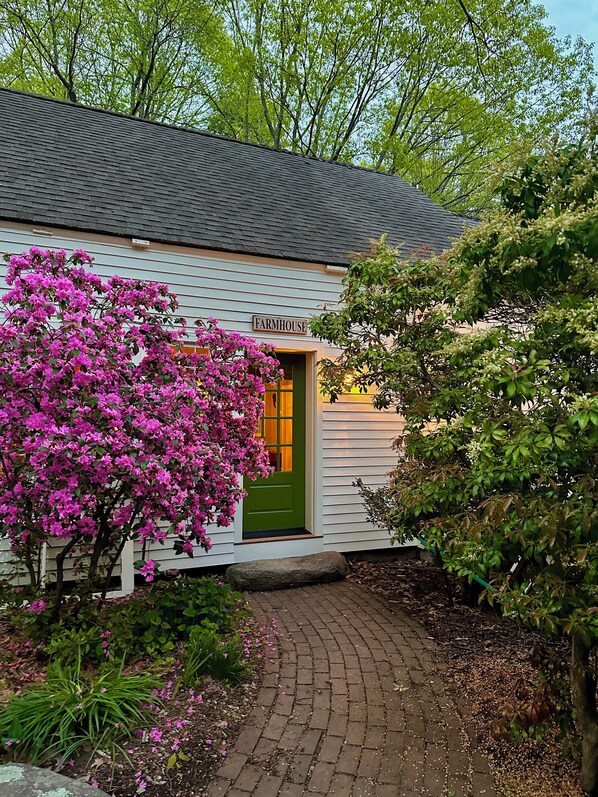 A farmhouse with a green door, surrounded by lush greenery and flowering plants. - The Farmhouse At Shilo Farm, 4 miles from Portsmouth, 10 minutes from the Beach (Eliot)