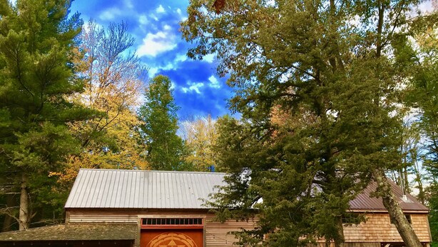 A rustic wooden building with a large circular door, surrounded by trees and a dirt path. - The Farmhouse At Shilo Farm, 4 miles from Portsmouth, 10 minutes from the Beach (Eliot)