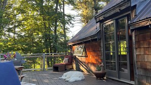 A wooden deck with outdoor furniture, a grill, and a building with large windows. - The Farmhouse At Shilo Farm, 4 miles from Portsmouth, 10 minutes from the Beach (Eliot)