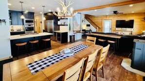 Een ruime keuken met een grote eettafel, houten kastjes en een kroonluchter.