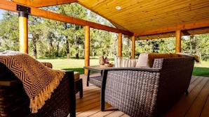 Een houten terras buiten met rieten meubels en een tafel, omringd door bomen.