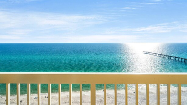 A beach view with a pier extending into the ocean, a clear sky, and a wooden railing in the foreground. - 3BR 2BA in tower 2 @ The Calypso, Closest Complex to Pier Park! (Panama City Beach)