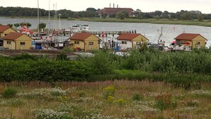 A marina with several yellow buildings, boats docked, and a river in the background. - thatched house, direct sea view, idyllic location in vacation region Usedom (Freest, Usedom)