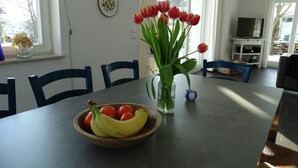 A dining area with a table set for two, featuring a bowl of fruit and a vase of tulips. - thatched house, direct sea view, idyllic location in vacation region Usedom (Freest, Usedom)