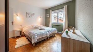 Makuuhuoneessa on sänky, yöpöydät, lipasto, ikkuna, jossa on verhot, ja ikkunasta avautuu näkymä ulos.