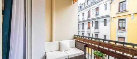 A balcony with a wicker sofa, a hanging plant, and a view of neighboring buildings.