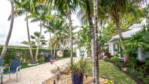 A patio with a stone floor, surrounded by palm trees and a garden with various plants and a large planter. - Tropical Paradise Beach Getaway, Villa #4 (Lauderdale-by-the-Sea)