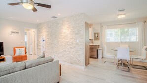 A modern living room with a stone accent wall, a ceiling fan, a dining area with a table and chairs, and a kitchen in the background. - Tropical Paradise Beach Getaway, Villa #4 (Lauderdale-by-the-Sea)