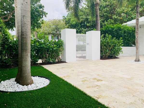 A landscaped garden with a paved walkway, a palm tree, and a white gate.